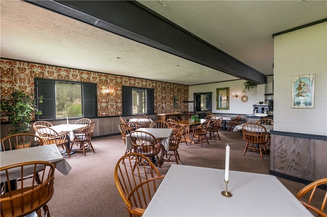 carpeted dining room with beamed ceiling, a textured ceiling, and wooden walls