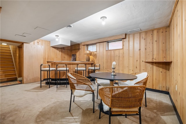 carpeted dining space featuring bar and wood walls