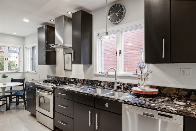 kitchen with hanging light fixtures, dark stone countertops, stainless steel appliances, sink, and wall chimney range hood