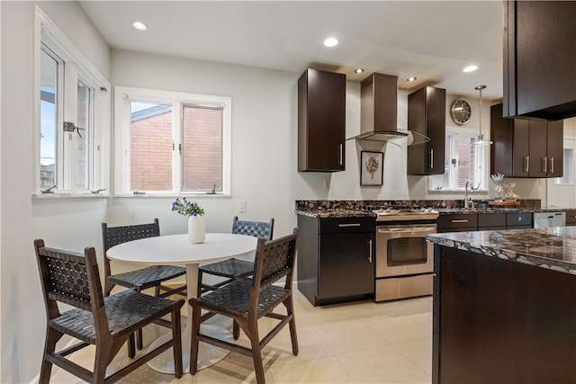 kitchen featuring wall chimney exhaust hood, dishwasher, pendant lighting, stainless steel gas range, and dark brown cabinetry