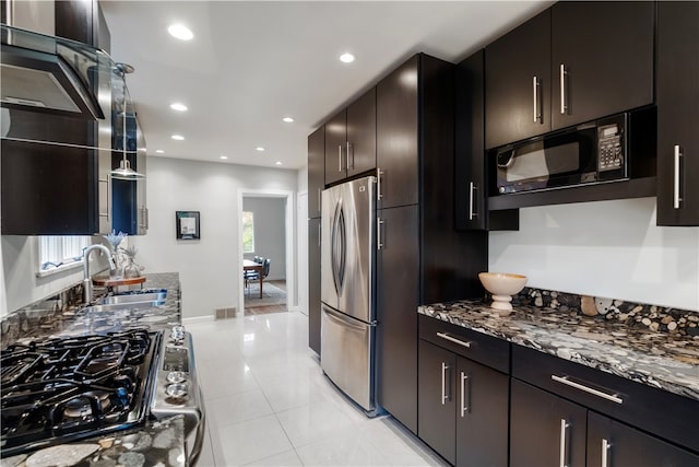 kitchen featuring appliances with stainless steel finishes, dark stone countertops, light tile patterned floors, dark brown cabinets, and sink