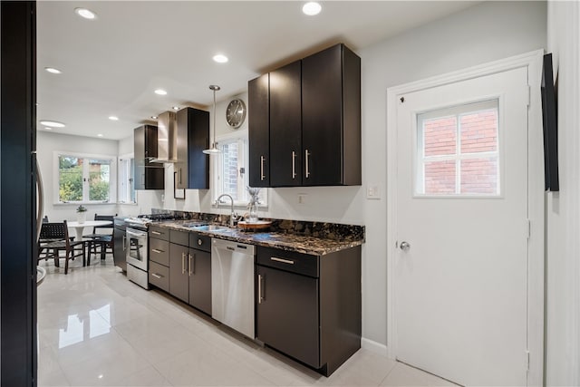 kitchen with pendant lighting, sink, wall chimney exhaust hood, appliances with stainless steel finishes, and dark stone counters