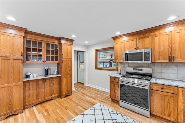 kitchen featuring light stone counters, decorative backsplash, appliances with stainless steel finishes, and light hardwood / wood-style flooring