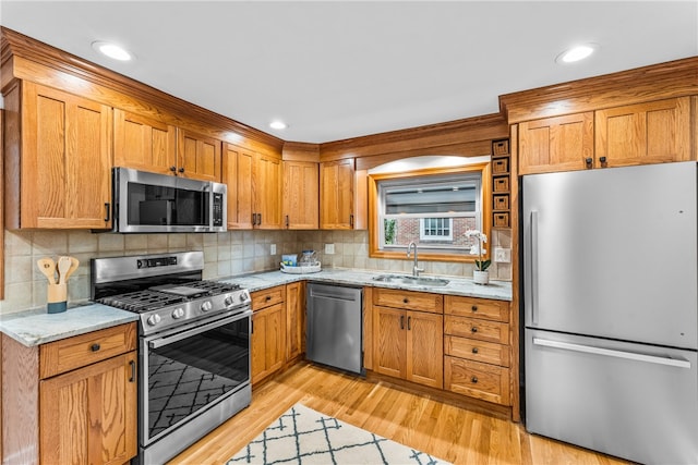 kitchen with appliances with stainless steel finishes, sink, light wood-type flooring, backsplash, and light stone counters