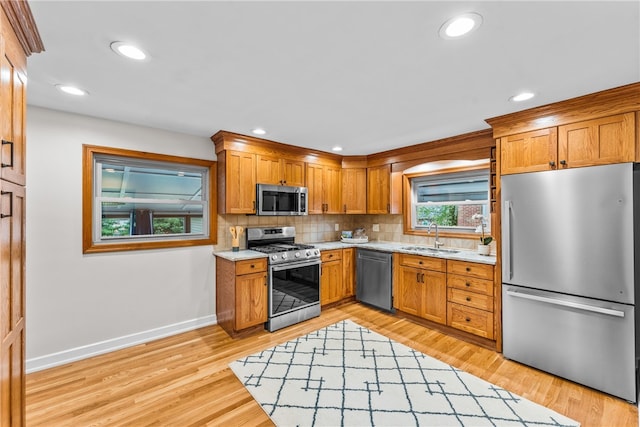 kitchen with appliances with stainless steel finishes, light hardwood / wood-style flooring, sink, and backsplash