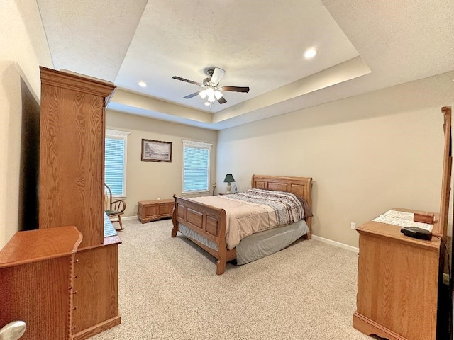 carpeted bedroom with a textured ceiling, a tray ceiling, and ceiling fan