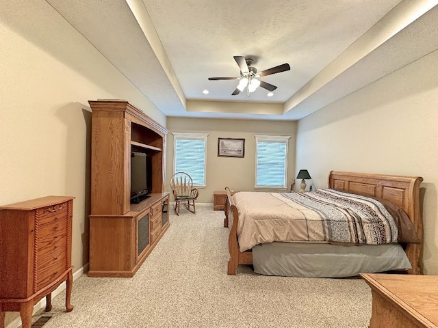 bedroom featuring ceiling fan, light colored carpet, a textured ceiling, and a raised ceiling