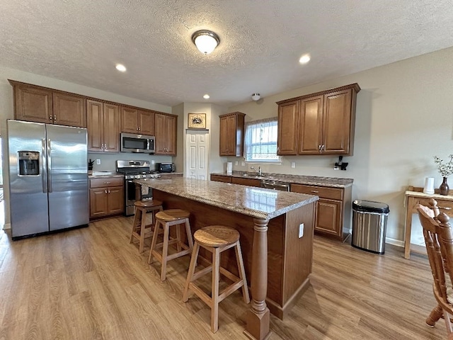 kitchen with light hardwood / wood-style floors, a kitchen island, stainless steel appliances, and light stone counters