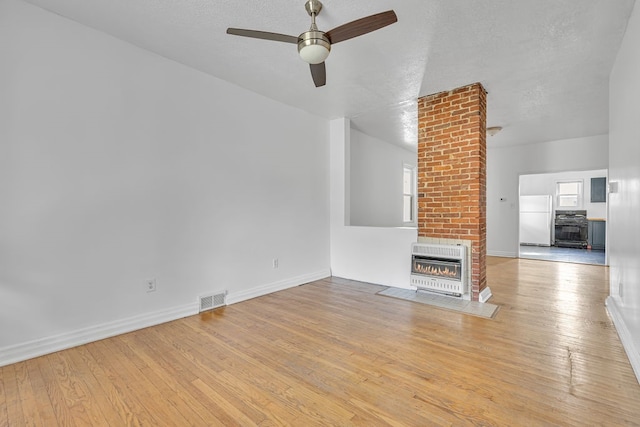 unfurnished living room featuring light wood-type flooring, heating unit, a textured ceiling, a brick fireplace, and ceiling fan