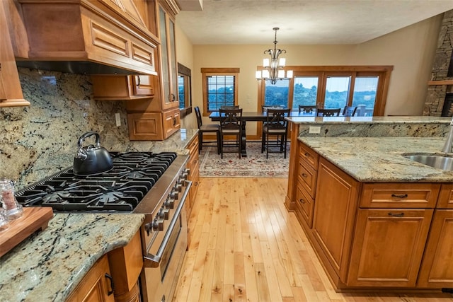 kitchen featuring light stone counters, custom exhaust hood, stainless steel range, pendant lighting, and light hardwood / wood-style floors