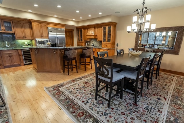 dining area featuring light wood-type flooring, sink, beverage cooler, and a chandelier