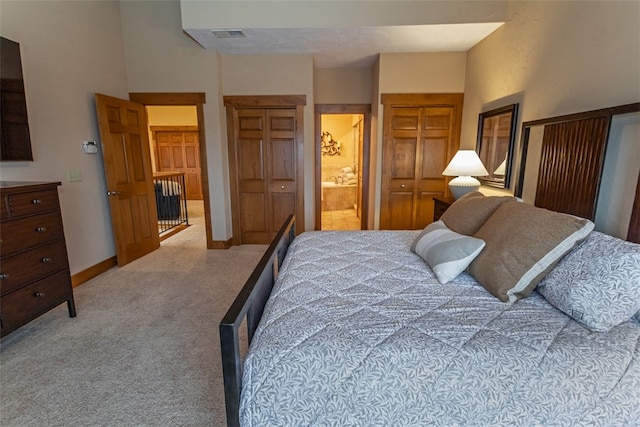 carpeted bedroom with ensuite bathroom, a high ceiling, and two closets