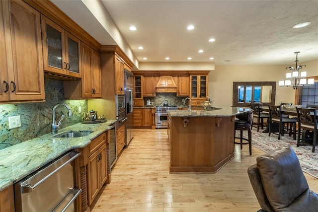 kitchen with hanging light fixtures, sink, light stone countertops, light wood-type flooring, and appliances with stainless steel finishes