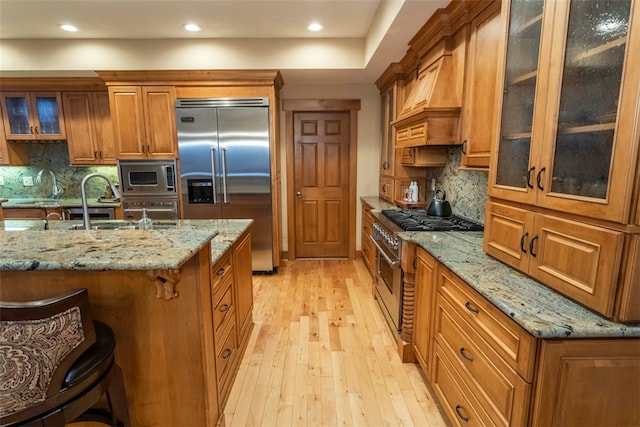 kitchen featuring built in appliances, light stone counters, light hardwood / wood-style flooring, and a breakfast bar