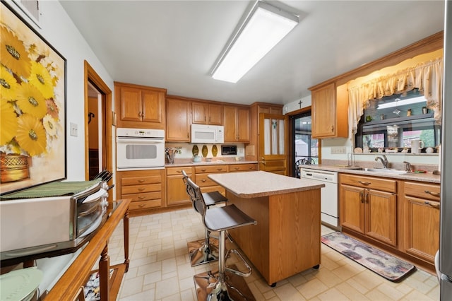 kitchen with a breakfast bar area, white appliances, a center island, and sink