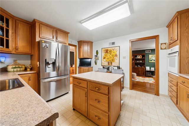 kitchen with oven, a kitchen island, sink, and stainless steel fridge with ice dispenser