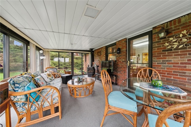 sunroom with wooden ceiling, a wood stove, and a healthy amount of sunlight