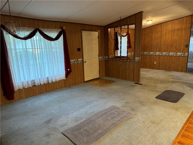 entrance foyer featuring carpet flooring, a notable chandelier, wood walls, and vaulted ceiling