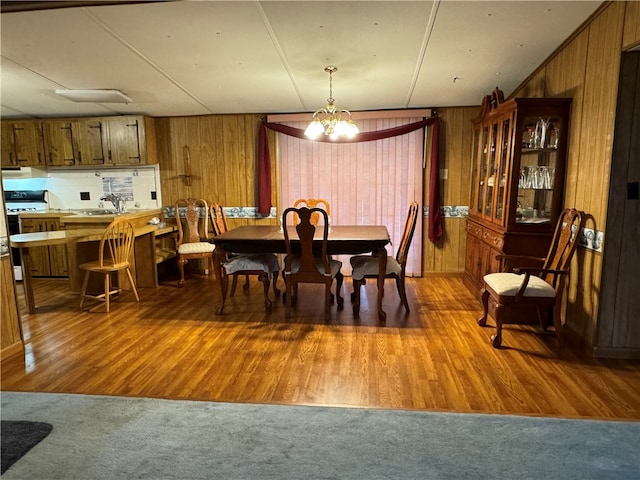 dining area with wood walls, an inviting chandelier, and hardwood / wood-style flooring