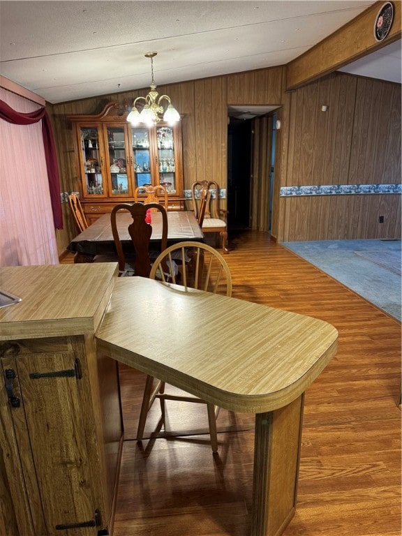 dining space with wood-type flooring, wooden walls, lofted ceiling, and a chandelier