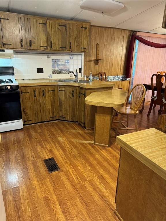 kitchen with decorative backsplash, hardwood / wood-style flooring, white range with gas cooktop, and sink