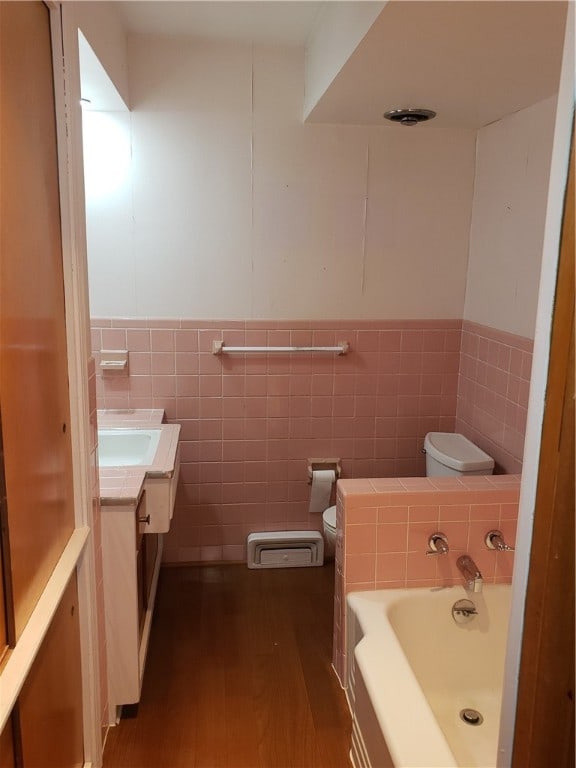 bathroom with tile walls, wood-type flooring, a washtub, vanity, and toilet