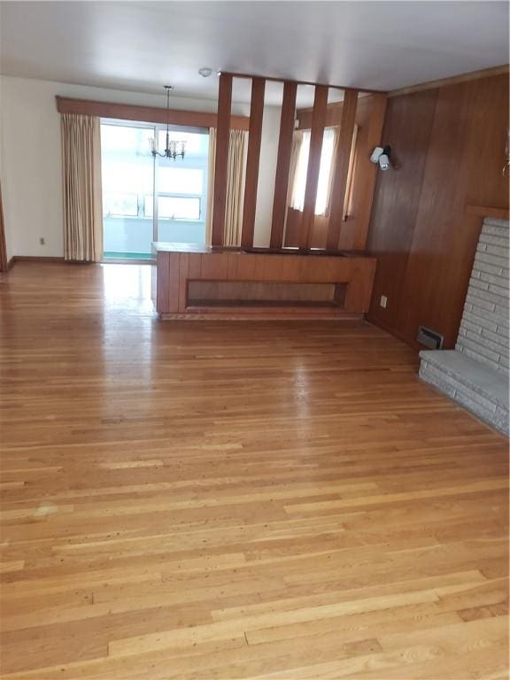 unfurnished living room featuring light wood-style floors, baseboards, a chandelier, and a fireplace with raised hearth