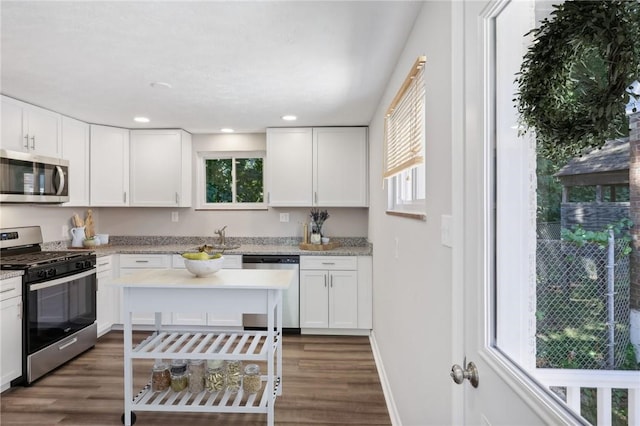 kitchen with light stone countertops, dark wood-type flooring, stainless steel appliances, and white cabinets