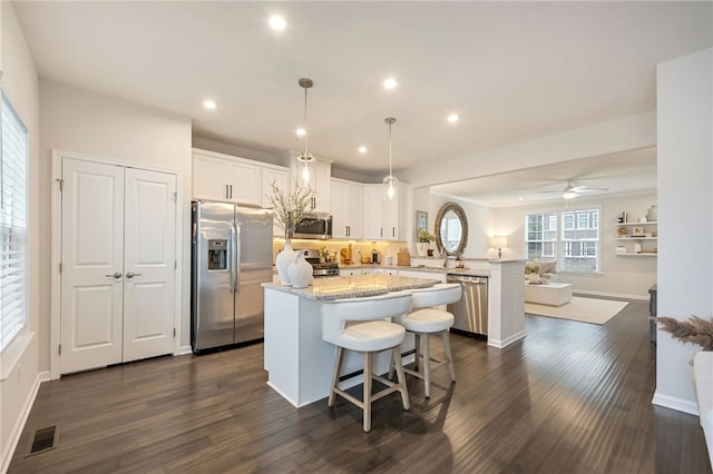 kitchen with dark wood-type flooring, white cabinets, kitchen peninsula, hanging light fixtures, and appliances with stainless steel finishes