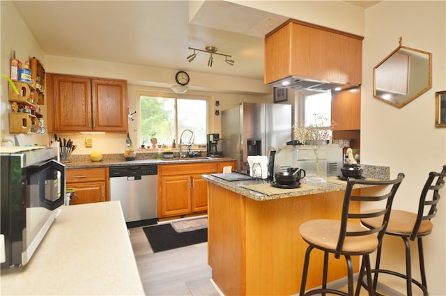 kitchen with a breakfast bar, sink, kitchen peninsula, appliances with stainless steel finishes, and light stone countertops