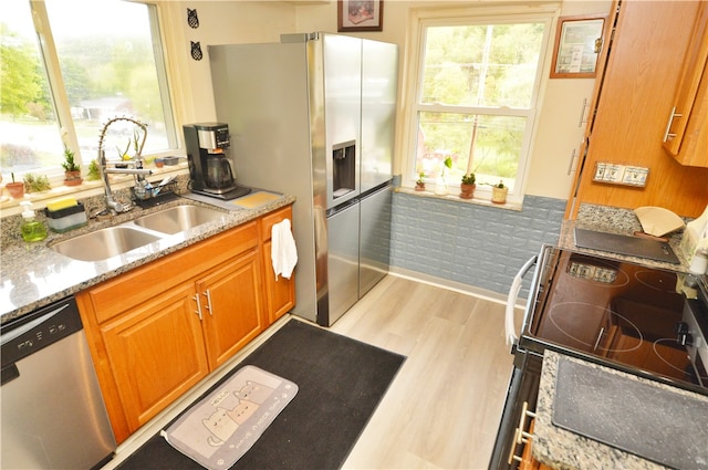 kitchen with light wood-type flooring, light stone counters, appliances with stainless steel finishes, and sink