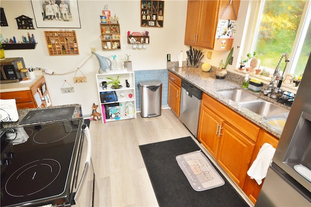 kitchen featuring light stone counters, appliances with stainless steel finishes, light wood-type flooring, and sink