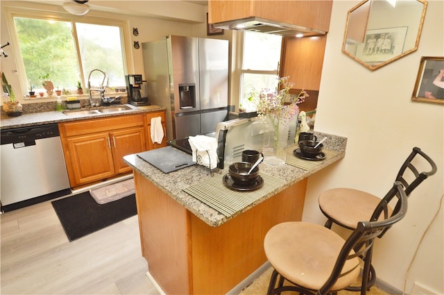 kitchen featuring light stone countertops, a breakfast bar area, stainless steel appliances, light hardwood / wood-style flooring, and sink