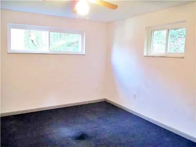 unfurnished room with dark carpet, ceiling fan, and plenty of natural light