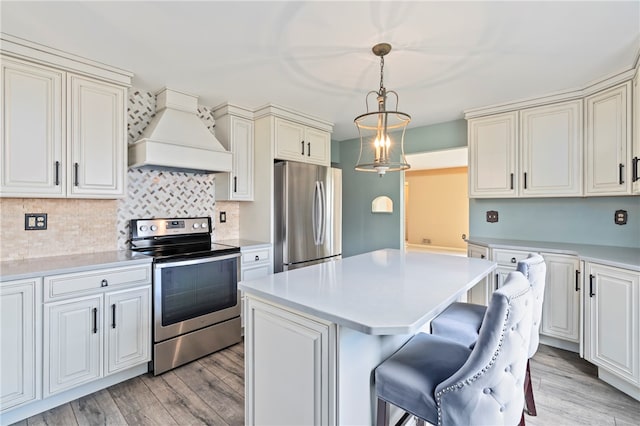 kitchen with decorative light fixtures, stainless steel appliances, custom range hood, a center island, and light hardwood / wood-style floors