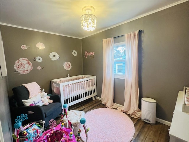 bedroom featuring dark wood-type flooring, a nursery area, a notable chandelier, and ornamental molding