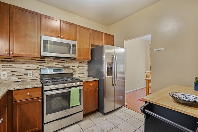 kitchen with stainless steel appliances, light stone counters, light tile patterned floors, and tasteful backsplash