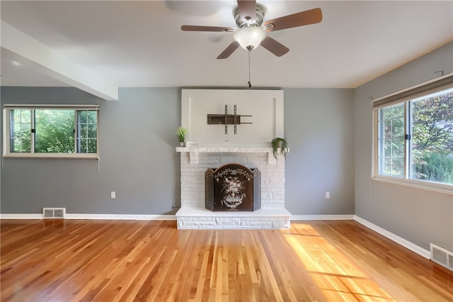 unfurnished living room with a fireplace, light wood-type flooring, a wealth of natural light, and ceiling fan