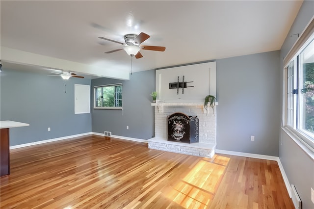 unfurnished living room with ceiling fan, hardwood / wood-style floors, a healthy amount of sunlight, and a brick fireplace