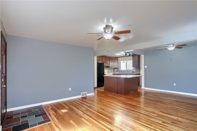 kitchen featuring a center island, backsplash, black fridge, light hardwood / wood-style flooring, and ceiling fan