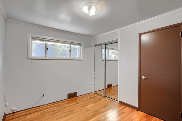 unfurnished bedroom with wood-type flooring, ornamental molding, and a closet