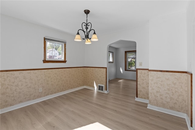 unfurnished room featuring a notable chandelier, plenty of natural light, and light hardwood / wood-style floors