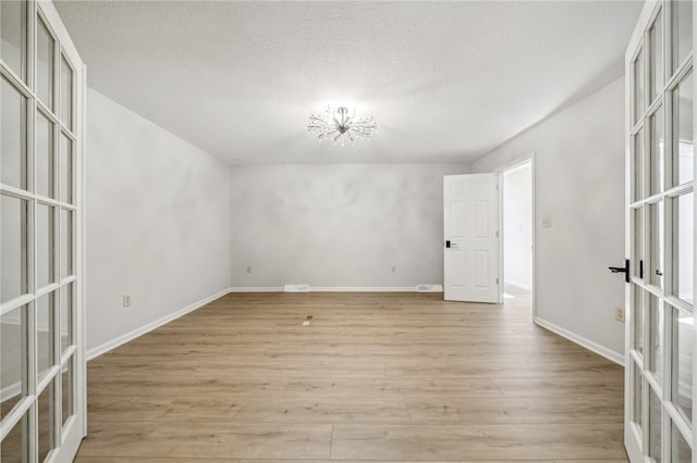 spare room featuring french doors, light wood-type flooring, a textured ceiling, and a notable chandelier