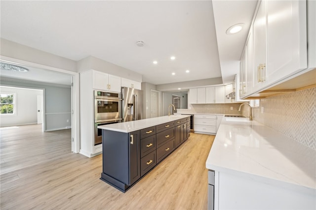 kitchen featuring white cabinets, light hardwood / wood-style flooring, a kitchen island, and appliances with stainless steel finishes