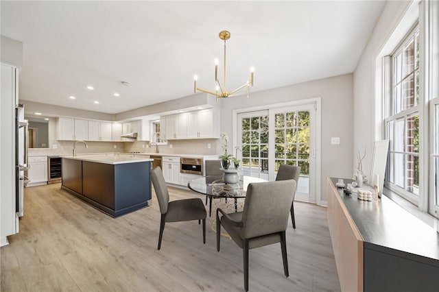 dining space featuring an inviting chandelier, light hardwood / wood-style flooring, beverage cooler, and sink