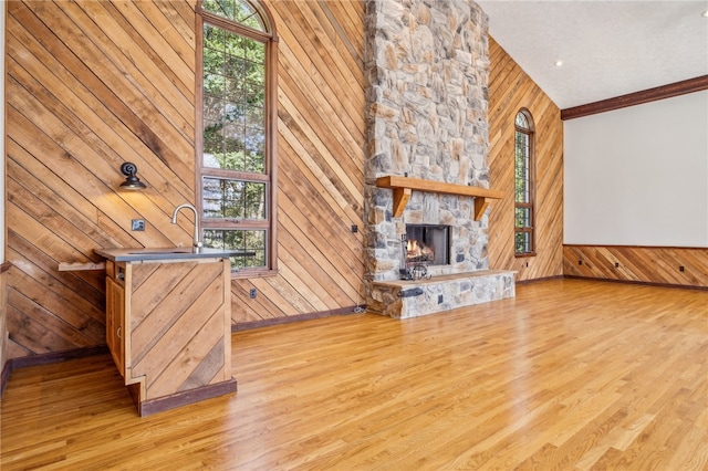 unfurnished living room with a towering ceiling, wooden walls, crown molding, hardwood / wood-style flooring, and a stone fireplace