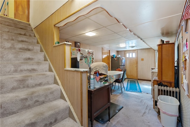 basement featuring light carpet, radiator, stainless steel refrigerator, and wooden walls