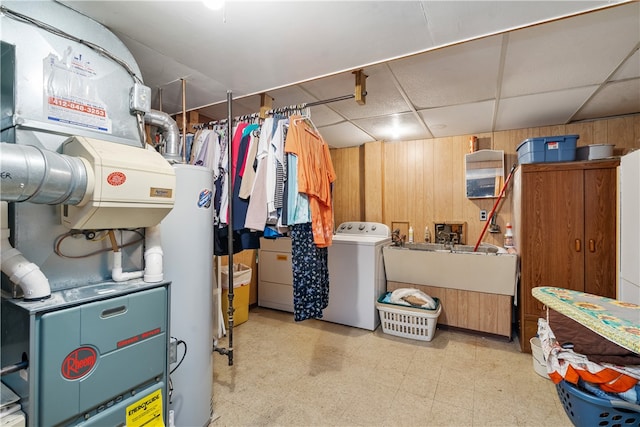 basement with a drop ceiling, wood walls, washing machine and clothes dryer, and gas water heater