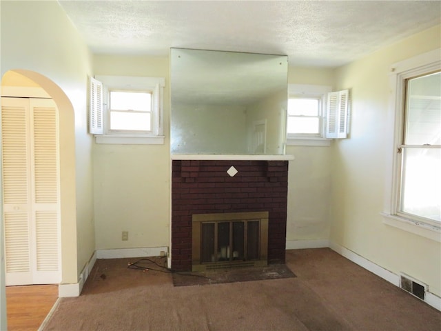 unfurnished living room with a brick fireplace, a textured ceiling, and carpet floors