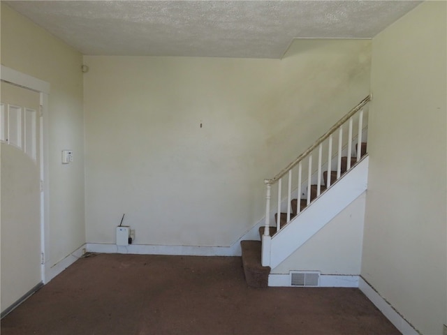 stairway with carpet floors and a textured ceiling